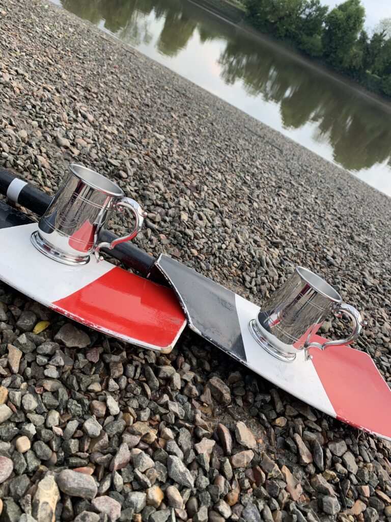 Two rowing tankards sitting on two sculling oars on a bank by the River Thames