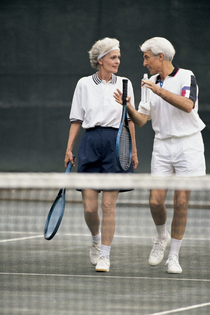 A man and woman with grey hair talking during a game of tennis