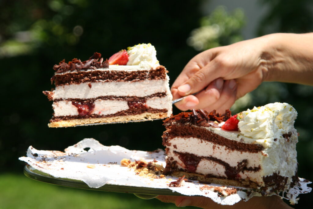 Slice of delicious cake with biscuit base, chocolate, marshmallows and cream being handed out